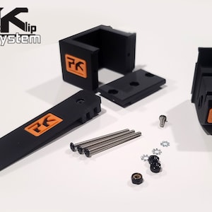 May include: A set of black plastic parts with orange "PK" logos, including two brackets, a lever, four screws, four washers, and two nuts. The parts are for a "Packlip System".