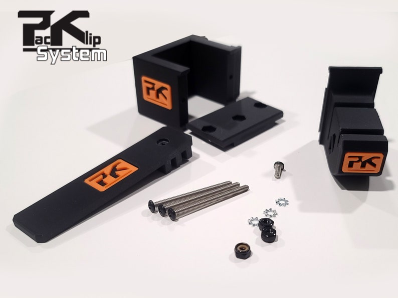 May include: A set of black plastic parts with orange "PK" logos, including two brackets, a lever, four screws, four washers, and two nuts. The parts are for a "Packlip System".
