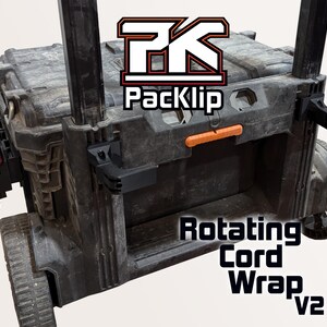 Peut inclure: Une bo&icirc;te &agrave; outils noire avec un enrouleur de cordon rotatif. La bo&icirc;te &agrave; outils a une poign&eacute;e orange et une batterie d'outil &eacute;lectrique noire et rouge fix&eacute;e sur le c&ocirc;t&eacute;. Le texte "Packclip" et "Rotating Cord Wrap v2" est visible sur la bo&icirc;te.