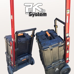 May include: Two black toolboxes with orange handles and a skull and crossbones design on the bottom box. The toolboxes are on a red and black rolling cart with a level attached to the side. The cart has a black handle and two black wheels. The text "Packlip System" is visible in the background.