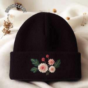 May include: A dark brown beanie with an embroidered floral design. The embroidery features pink and white flowers, green leaves, and red berries. The text "ECOCHICCRAFT" is visible on the top left of the beanie.