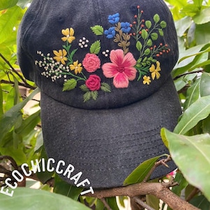 May include: A dark gray baseball cap with embroidered flowers in yellow, pink, and blue. The floral design is on the front of the cap. The text "ECOCHIC CRAFT" is printed on the brim.