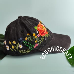 May include: A black denim baseball cap with embroidered flowers in shades of orange, pink, yellow, and green. The text "Ecochiccraft" is embroidered on the side of the cap.