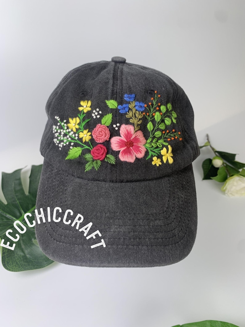 May include: A dark gray baseball cap with embroidered flowers in pink, red, yellow, and blue. The text "ECOCHIC CRAFT" is printed in white on the brim. The cap has a curved brim and a button on top.