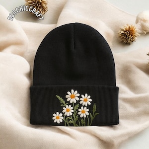 May include: A black beanie with a folded brim, embroidered with a cluster of white daisies with yellow centers and green stems and leaves. The text "ECOCHIC CRAFT" is printed on the top left of the image.