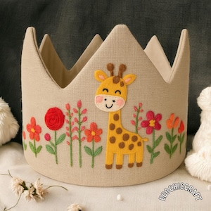 May include: A beige fabric crown with a giraffe applique and embroidered flowers. The giraffe is yellow with brown spots. Red, pink, and orange flowers are embroidered around the base of the crown. The crown has a pointed top.