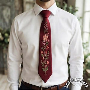 May include: A crisp white button-down shirt paired with a deep burgundy necktie. The tie features a vertical, centred embroidery of delicate wildflowers in shades of pink, peach, and green, extending from the knot down to the pointed tip.