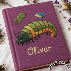 Puede incluir: Un diario morado con un diseño de oruga bordada. La oruga es verde, amarilla y naranja. El nombre "Oliver" está bordado en cursiva. Una pequeña hoja y un libro bordados también están en la portada.