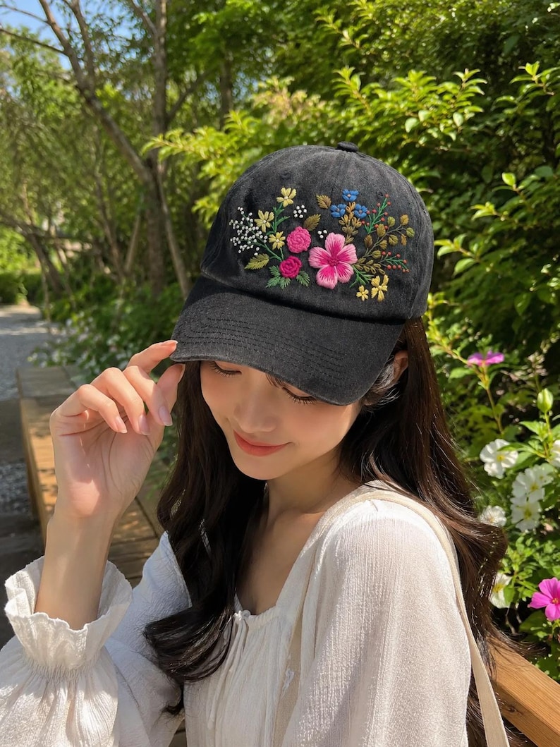 May include: Black baseball cap with embroidered floral design. The cap features a curved brim and a colorful floral arrangement on the front, including pink, yellow, and blue flowers. The cap is made of a soft fabric.