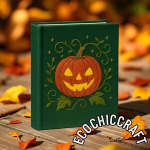 May include: A dark green hardcover book featuring an embroidered orange jack-o'-lantern pumpkin with yellow eyes and a mouth, surrounded by green embroidered vines, leaves, and small yellow stars on the front cover.