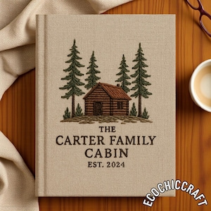 May include: A beige linen journal with an embroidered cabin scene. The design features a brown cabin, green pine trees, and the text "THE CARTER FAMILY CABIN EST. 2024". The journal is a personalized keepsake.