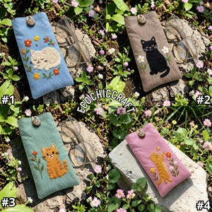 May include: Four rectangular fabric eyeglass cases featuring embroidered cat designs and wooden button closures. Each case displays a unique cat illustration surrounded by floral motifs in blue, tan, green, and pink fabric colors.