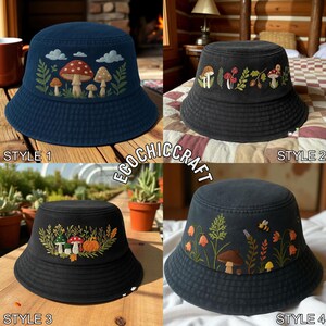 May include: Four dark-colored bucket hats featuring embroidered nature designs. Style 1 shows mushrooms and clouds. Style 2 displays mushrooms and acorns. Style 3 depicts mushrooms and a pumpkin. Style 4 features wildflowers, a mushroom, and a bee.