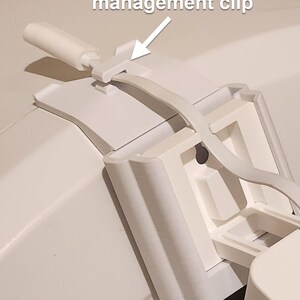 May include: Close-up of a white plastic cable management clip. The clip is designed to hold a cable in place. The text "Built-in cable management clip" is visible in the image.