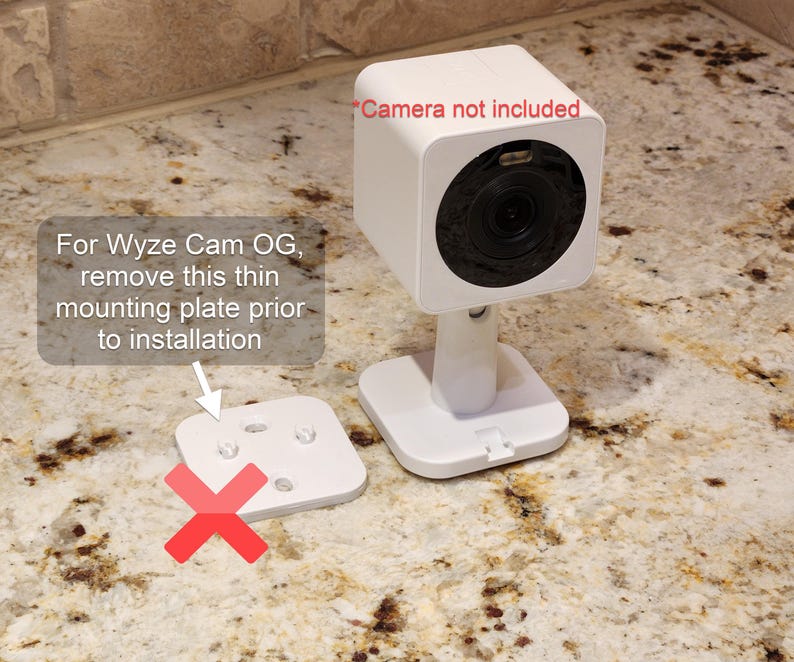 May include: A white Wyze Cam OG security camera with a square design, mounted on a stand. The image includes text that says "Camera not included" and instructions to remove a mounting plate before installation.