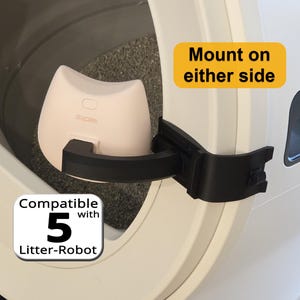 May include: A light pink cat-shaped device with the text 'sipet' attached to a black mounting arm on a white Litter-Robot. The device features a yellow label stating 'Mount on either side' and a white label stating 'Compatible with 5 Litter-Robot'.