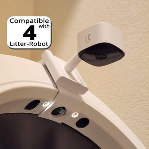 May include: A white security camera, branded "eufy SECURITY", is mounted on a white bracket. The bracket is attached to a white surface. The image also includes the text "Compatible with 4 Litter-Robot".