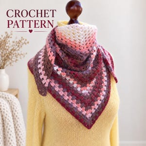 Peut inclure: Un châle triangulaire au crochet présentant un dégradé de couleurs incluant crème, rose tendre, magenta profond et brun foncé. Le châle est présenté sur un pull jaune et inclut le texte CROCHET PATTERN avec une petite icône de cœur au-dessus.