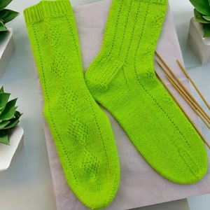 Pode incluir: Um par de meias de lã verde limão com um padrão de renda. As meias estão dispostas sobre uma superfície branca.