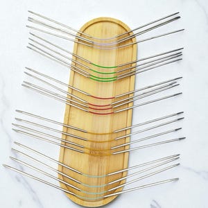 May include: A collection of circular knitting needles with stainless steel tips and flexible, color-coded cables. The needles are arranged on a light brown wooden tray, with the cables in purple, green, red, yellow, and teal.