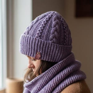 May include: A matching lavender knitted hat and scarf set. The hat features a cable knit design and a ribbed brim. The scarf is a long, rectangular shape with a simple knit pattern. A small leather tag is attached to the hat.