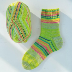 Peut inclure: Une chaussette vert vif avec des rayures color&eacute;es et une pelote de laine assortie. La chaussette pr&eacute;sente des bandes roses, bleues et jaunes, cr&eacute;ant un aspect joyeux et fait main. La pelote de laine compl&egrave;te la chaussette avec des teintes similaires, parfait pour les projets de tricot.