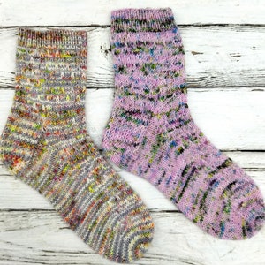 Puede incluir: Dos pares de calcetines de punto coloridos. Un par es gris con motas multicolores y el otro par es rosa con motas multicolores.