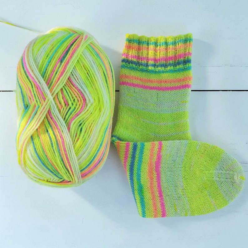 Peut inclure: Une chaussette tricot&eacute;e &agrave; la main et une pelote de laine assortie. La chaussette et la laine sont principalement vert fluo, avec des rayures roses, jaunes, bleues et blanches. La laine est une pelote douce et textur&eacute;e, et la chaussette est de longueur standard.