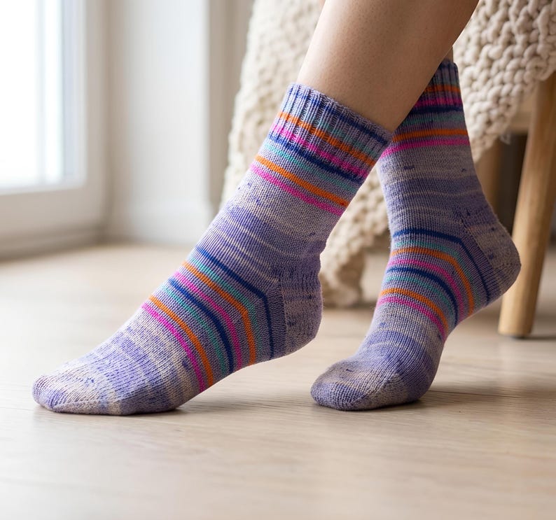 Peut inclure: Une paire de chaussettes lavande avec des rayures horizontales color&eacute;es dans les tons de rose, orange, bleu et sarcelle. Les chaussettes sont port&eacute;es aux pieds d'une personne, les jambes &eacute;tant visibles des chevilles vers le bas. Les chaussettes sont en tricot doux.