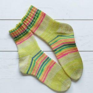 Peut inclure: Une paire de chaussettes tricot&eacute;es &agrave; la main aux couleurs vives. Les chaussettes pr&eacute;sentent une base vert clair avec des rayures horizontales roses, oranges, bleues et vertes. Les poignets et les orteils ont un motif de couleurs plus concentr&eacute;.