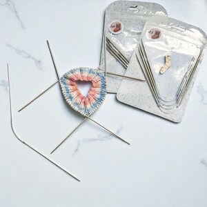 Puede incluir: Suministros de tejido que incluyen agujas circulares y un calcet&iacute;n parcialmente tejido en rosa, azul y blanco. Se ven dos juegos de agujas empaquetadas, junto con agujas individuales para tejer.