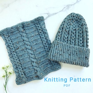 May include: A knitted blue hat and cowl set with a cable knit design. The set is made of speckled yarn and is displayed on a white marble surface. The text "Knitting Pattern PDF" is visible in the image.