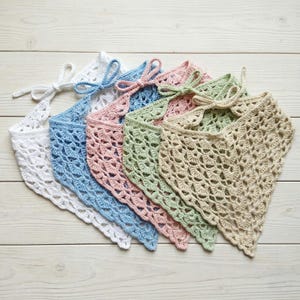 May include: A collection of six handmade crochet bandanas in various pastel colors, including white, blue, pink, green, and beige. Each bandana features a delicate openwork design and a tie closure at the neck, perfect for a stylish accessory.