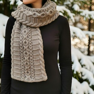May include: A knitted scarf in shades of gray and brown, featuring intricate cable and diamond patterns. The scarf is wrapped around the neck and chest, with a textured design. The background shows a snowy, blurred forest.