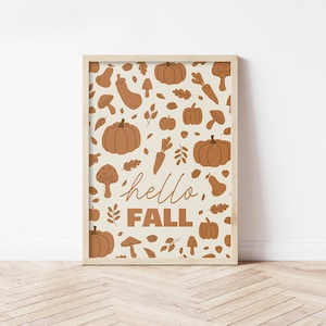 Könnte beinhalten: Ein gerahmter Druck mit beigem Hintergrund, verziert mit einem sich wiederholenden Muster aus braunen Kürbissen, Pilzen, Blättern, Karotten und Birnen. Die Worte "hello, FALL" sind in Schreibschrift geschrieben. Der Rahmen ist hellbraun.