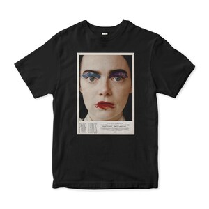 May include: Black t-shirt with a poster design featuring a woman with blue and purple makeup and the text "Poor Things".