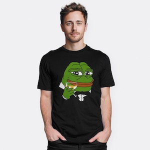Pode incluir: Uma camiseta preta com um desenho de um sapo verde de smoking, segurando um copo de líquido. O sapo tem uma expressão satisfeita no rosto.