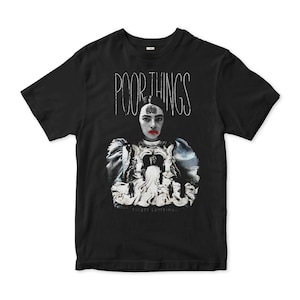 May include: Black t-shirt with a white graphic of a woman in a white dress with the text "POOR THINGS" and "...forget everything."