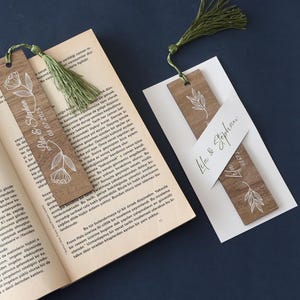 Puede incluir: Marcadores de madera con dise&ntilde;os florales y de hojas, y borlas verdes. Un marcador tiene los nombres "Lila & Stephan" y la fecha "08.07.2025" impresos. Los marcadores est&aacute;n colocados sobre un libro.