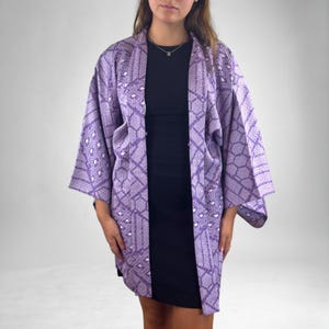 Puede incluir: Una chaqueta estilo kimono lavanda con un patr&oacute;n geom&eacute;trico. La chaqueta abierta tiene mangas anchas y un ajuste relajado. El patr&oacute;n incluye formas de diamante y hexagonales en un tono m&aacute;s claro de lavanda y blanco.