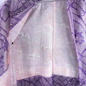 Puede incluir: Un kimono vintage con un exterior estampado en morado y blanco y un interior rosa claro. El interior presenta un dise&ntilde;o de p&aacute;jaros y olas blancos. Los bordes del kimono est&aacute;n adornados con un patr&oacute;n geom&eacute;trico morado m&aacute;s oscuro.