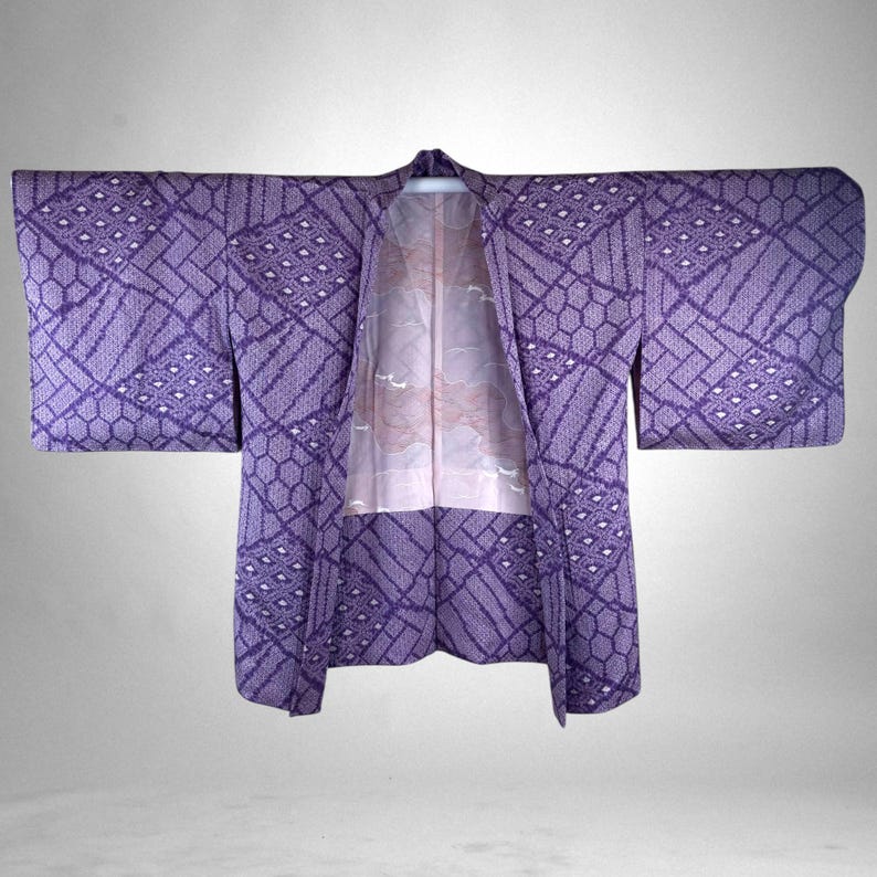 Puede incluir: Un kimono japon&eacute;s tradicional en tonos morados, con patrones geom&eacute;tricos y de diamantes. El forro interior del kimono es rosa claro con un dise&ntilde;o floral. Las mangas est&aacute;n extendidas.