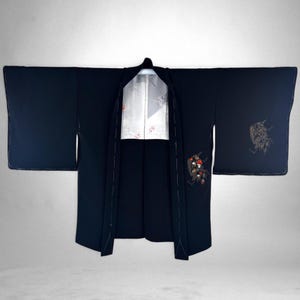 May include: A dark navy blue kimono with wide sleeves, open to reveal a white and silver patterned lining. The kimono features embroidered floral and geometric designs in red, black, and gold.