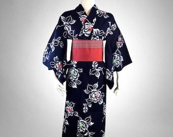 May include: A navy blue yukata with a floral pattern of white and red flowers. The traditional Japanese garment features wide sleeves and is cinched at the waist with a red obi sash. The yukata is displayed on a mannequin.