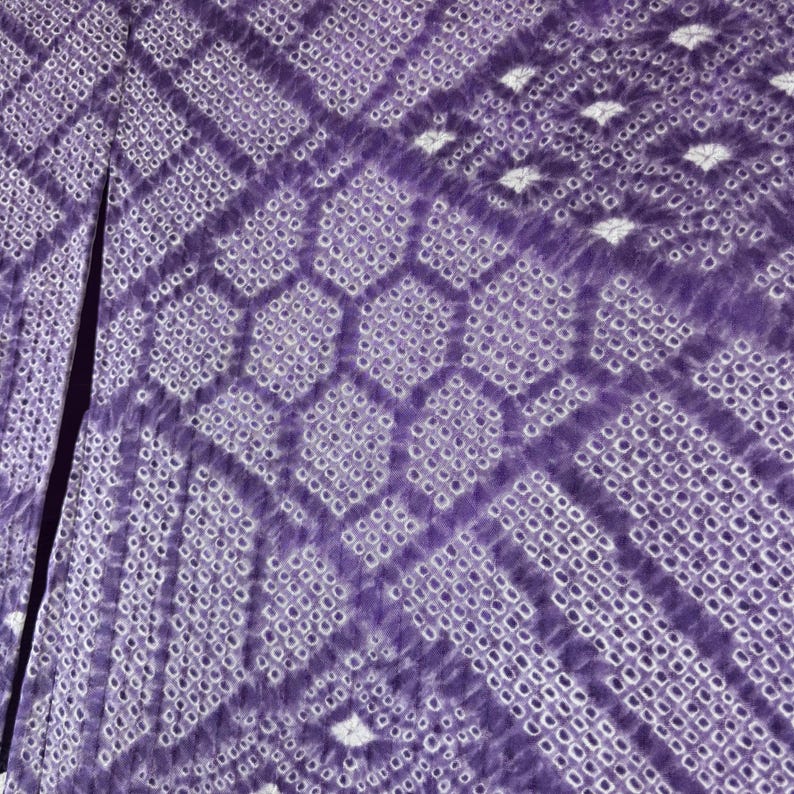 Puede incluir: Primer plano de una tela morada con un patr&oacute;n geom&eacute;trico. El dise&ntilde;o presenta una combinaci&oacute;n de formas de diamante y hexagonales, con una textura punteada. La tela tiene una abertura en el medio, revelando un interior m&aacute;s oscuro.