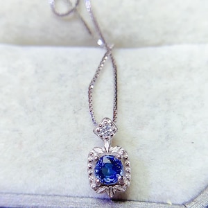 Op de afbeelding: Een zilveren ketting met een blauwe saffier hanger in een vierkant frame met kleine diamanten rond de randen.