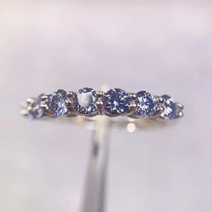 Peut inclure: Une bague en argent ornée de cinq pierres bleues rondes. Les pierres sont disposées en ligne et scintillent. Le design de la bague est simple, mettant en valeur l'éclat des pierres bleues. L'arrière-plan est flou.