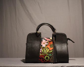 May include: Black leather handbag with a colorful floral embroidered panel and a tassel.