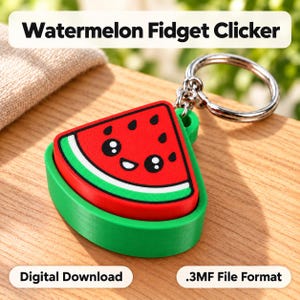 May include: A watermelon-shaped fidget clicker keyring featuring a red slice with black seeds, a white rind, and a green base. The top surface displays a smiling face with large black eyes. The object includes a silver metal ring attachment.