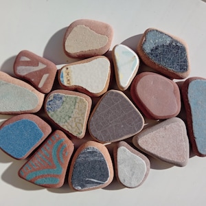 Peut inclure: Une collection de 13 pierres lisses, colorées et à motifs. Les pierres sont de différentes nuances de brun, bleu, vert et blanc. Certaines pierres ont une surface texturée.